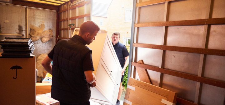 Vue depuis l'intérieur d'un grand camion de deux déménageurs en train de charger une armoire.