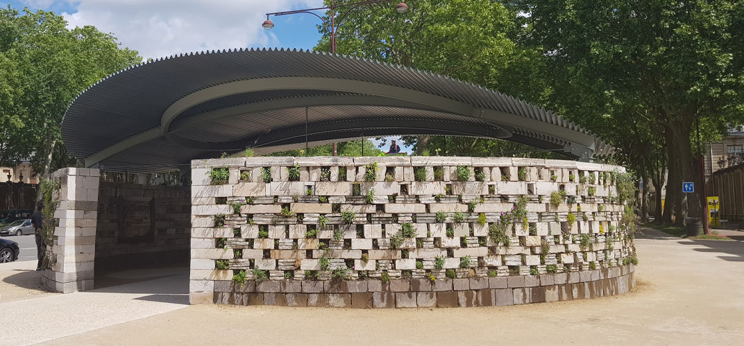 Biennale de l'architecture Ile de France 2022 : Vue du pavillon circulaire élaboré par l’agence ChartierDalix est constitué d’un immense mur de pierre habité par la faune et la flore sur sa face extérieure.