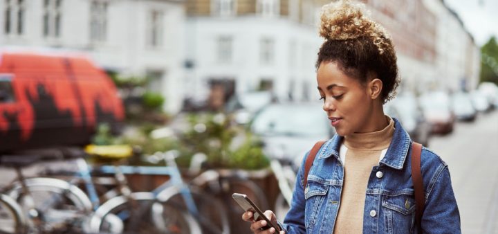 Une jeune femme en centre-ville, smartphone en main. Interview du sociologue Julien Damon sur le changement de paradigme de la « ville intelligente » gouvernée par l’IA.