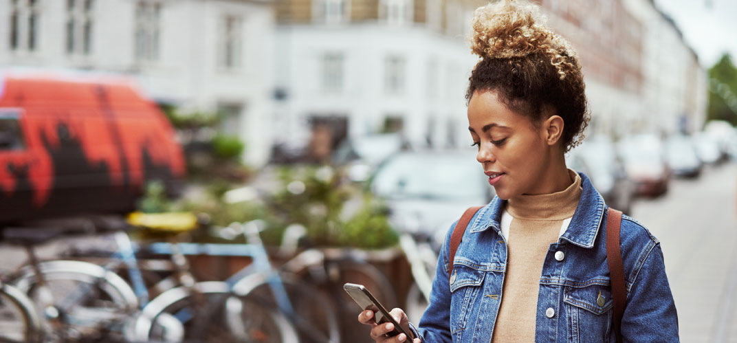 Une jeune femme en centre-ville, smartphone en main. Interview du sociologue Julien Damon sur le changement de paradigme de la « ville intelligente » gouvernée par l’IA.