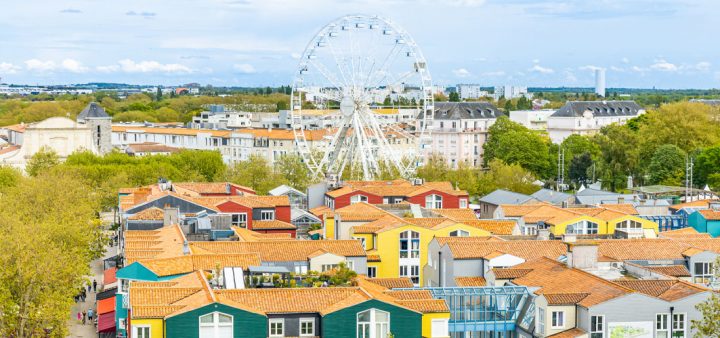 Un village coloré avec une grande roue de fête foraine en arrière-plan. Décryptage du label BBCA Quartier qui vient compléter la labellisation Bâtiment Bas Carbone ou encore BBCA Rénovation.