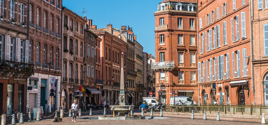 Vue du centre-ville de Toulouse : une place de la ville rose avec une fontaine en son centre.