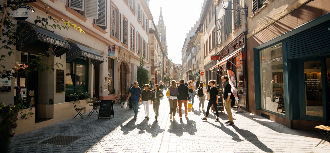 Promeneurs dans une rue bordées de commerces d'un centre-ville.