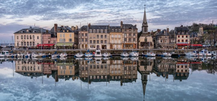 Risques de submersion sources et carte : vue du port d'Honfleur se reflétant dans l'eau sous un ciel nuageux.