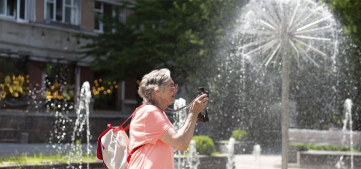 Economies d'eau en ville : Une femme âgée photographiant des fontaines et jeux d'eau sur une place par une chaude journée d'été.