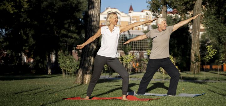 Un couple de seniors pratiquant le yoga sur la pelouse d'un parc de centre-ville.