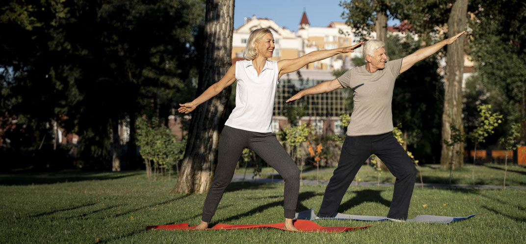 Un couple de seniors pratiquant le yoga sur la pelouse d'un parc de centre-ville.