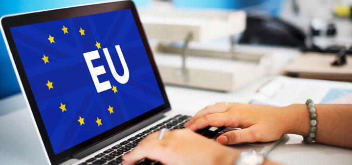 Plan serré sur des mains travaillant à l'ordinateur, avec le drapeau de l'union européenne.