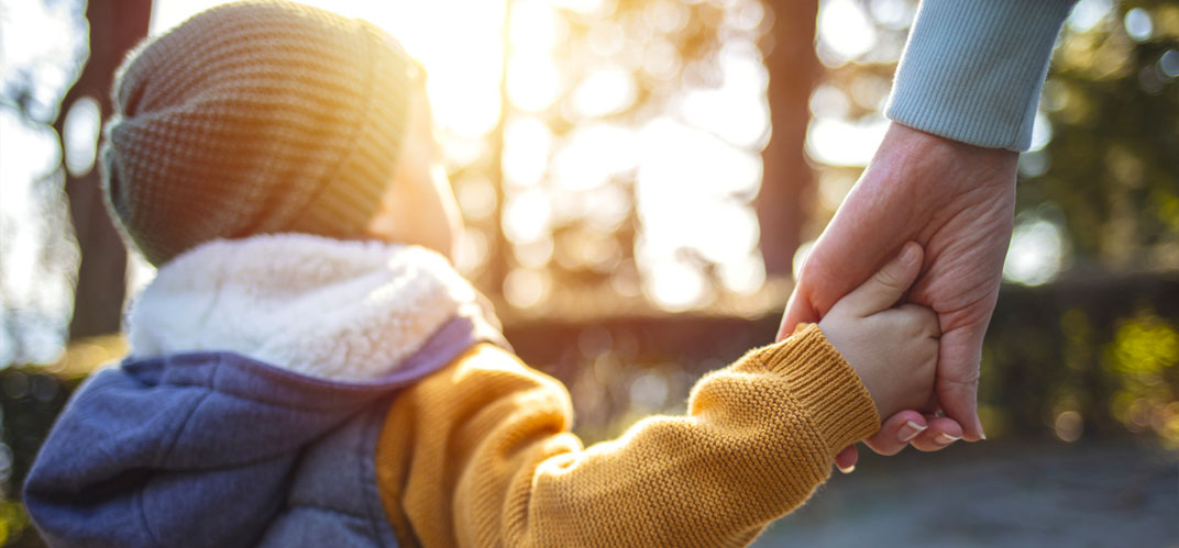 Ville à hauteur d'enfants : un bambin de dos tenant la main d'un adulte.