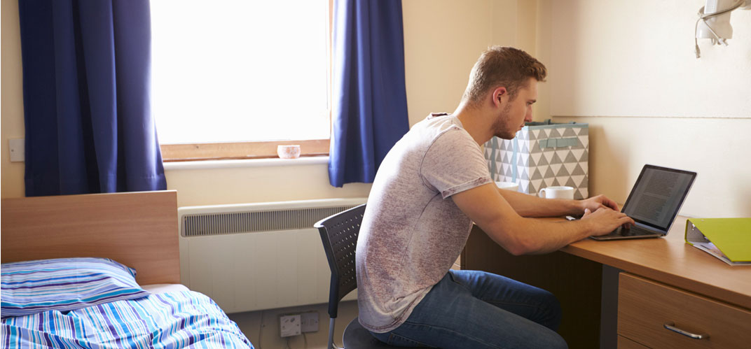 Crise du logement chez les jeunes : un jeune homme à son bureau dans une chambre exigue.